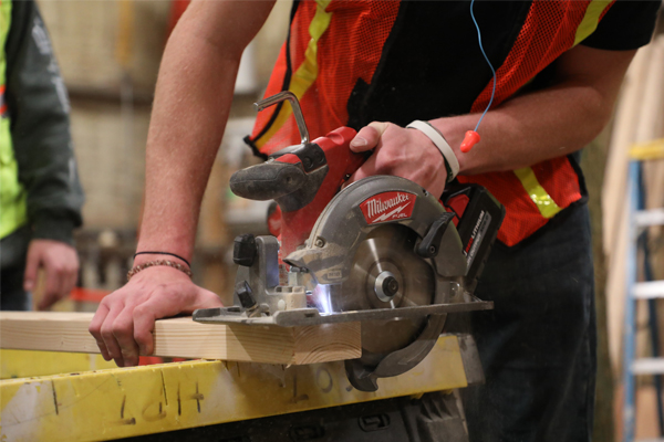 A student using a hand saw to cut wood.