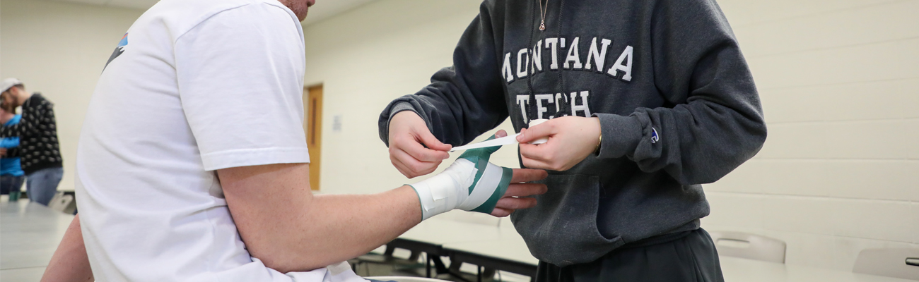 Student taping someone's hand with pre-wrap and tape