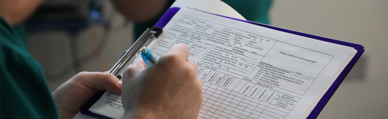 Nursing simulation student writing notes on a clipboard