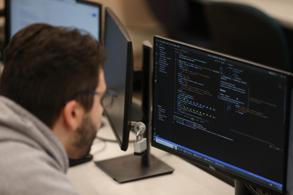 Male student looking at a computer monitor with program code