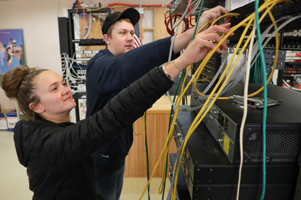 Man and a woman plugging in cables into a network switch