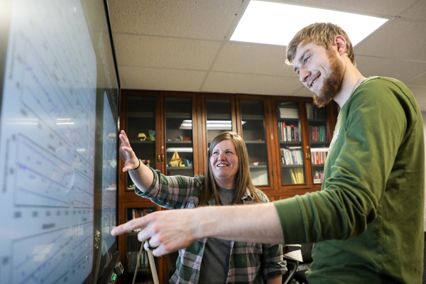 Man and a woman looking at graphs displayed on a smartboard