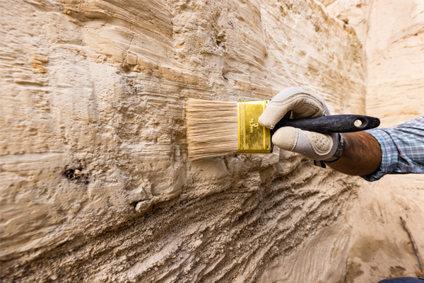 Hand using a brush on a dirt wall