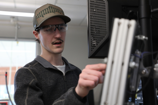 Man wearing safety glasses pointing at a computer monitor