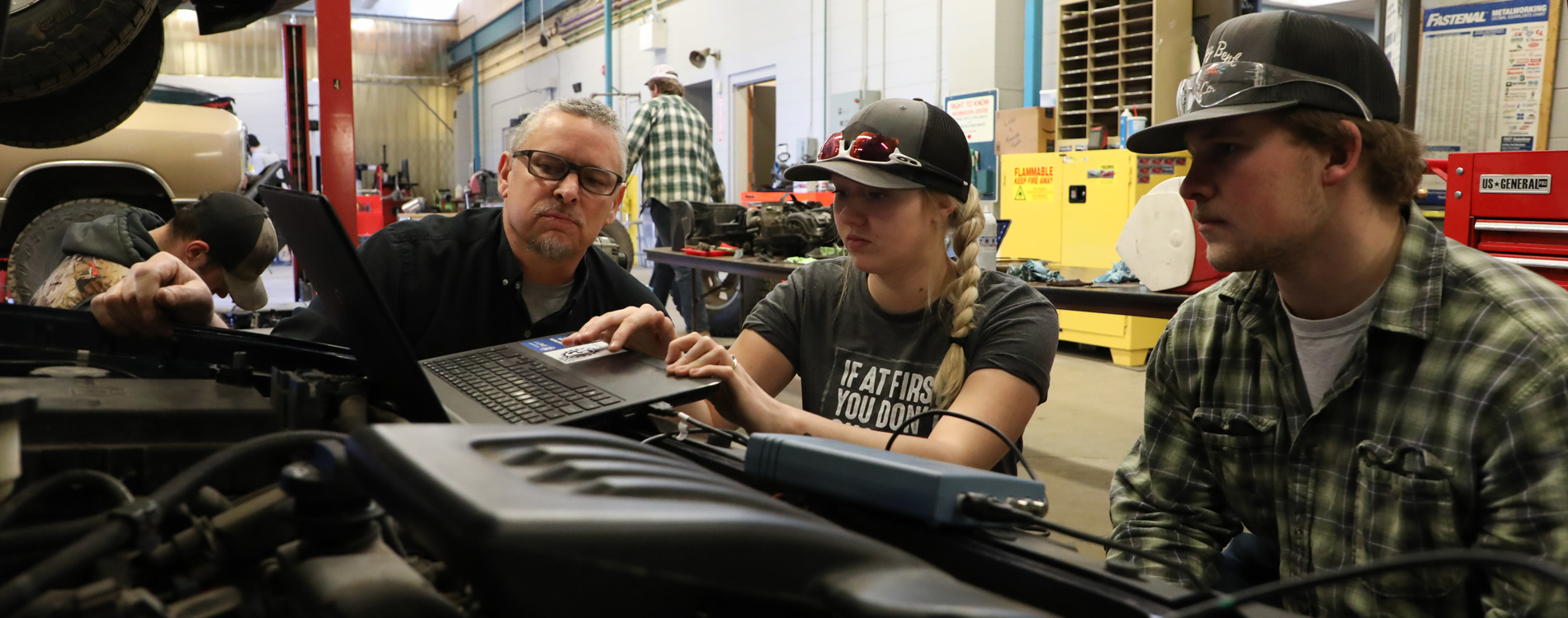 Three people working on a car in auto lab. 
