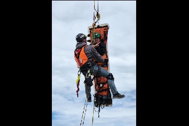 Two people hang from a hoist in safety gear