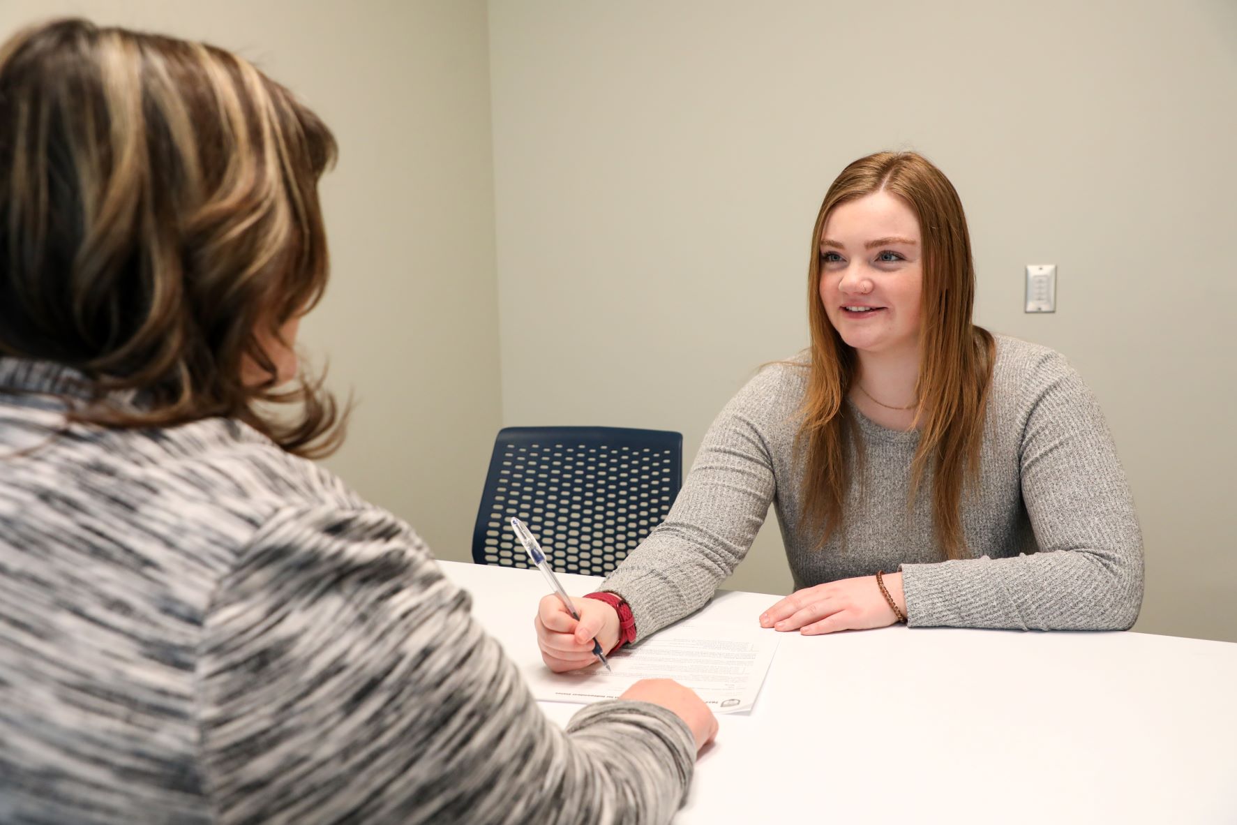 Female student sitting at a desk about to sign a document.