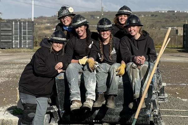 A group of female students in mining gear pose together in a mine cart.
