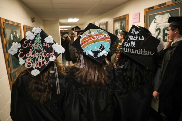 !Three decorated graduation caps are worn by students