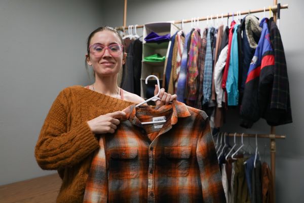Cheyenne Crooker holds up a plaid shirt in front of racks of clothing