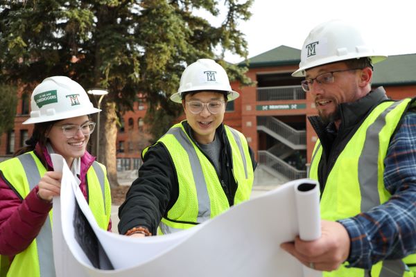 Two students in hard hats look at a blue print