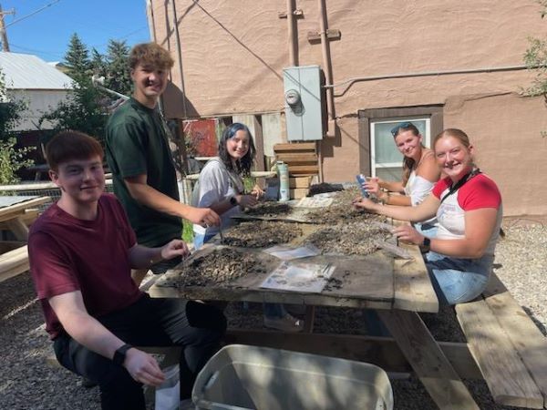 Student appear to be digging through rocks at a picnic table as part of the summer bridge program. 