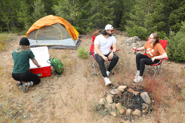 Two women and a man sitting around a fire pit